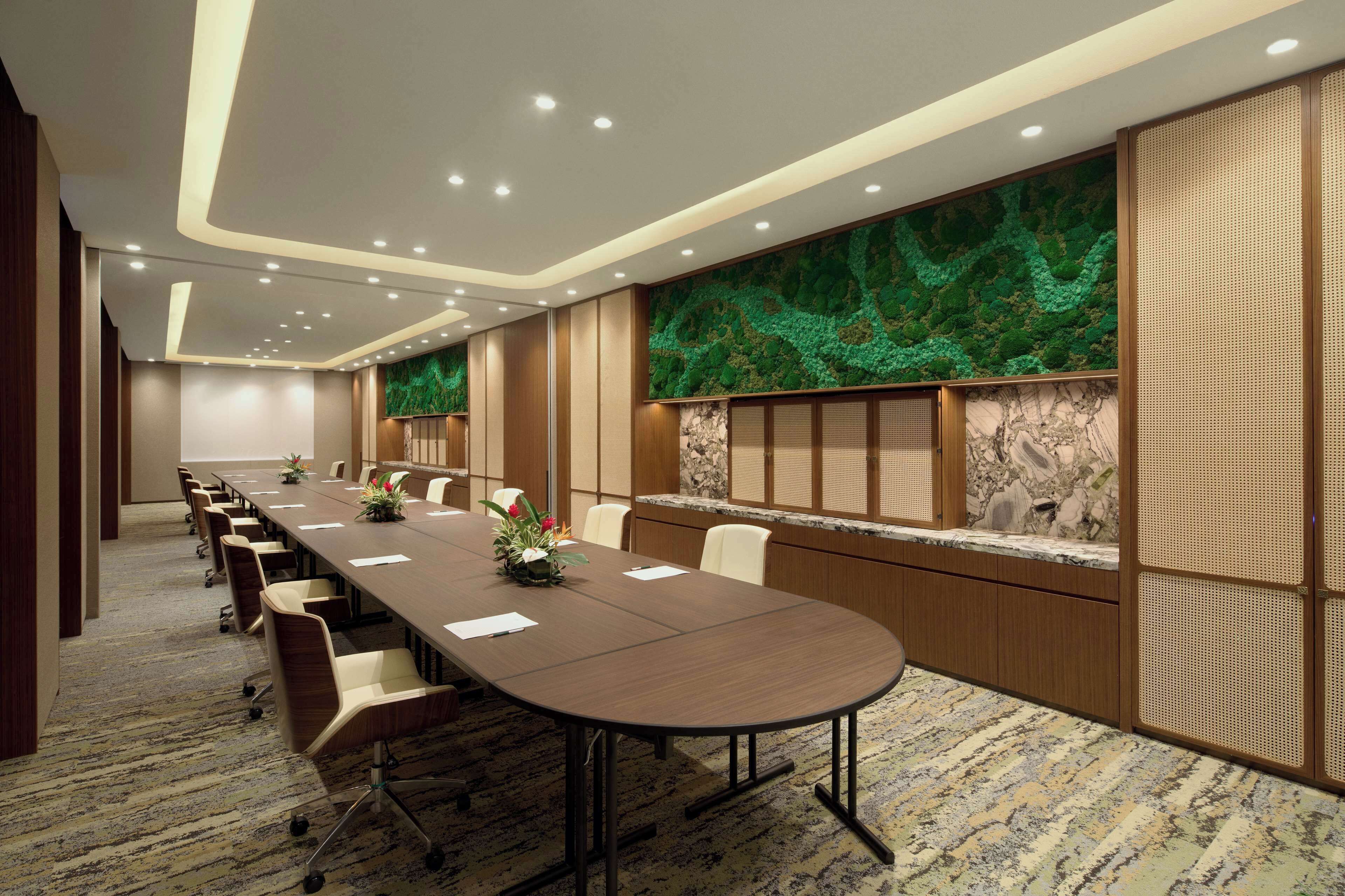Uma sala de conferências com uma mesa comprida, cadeiras e um painel decorativo.