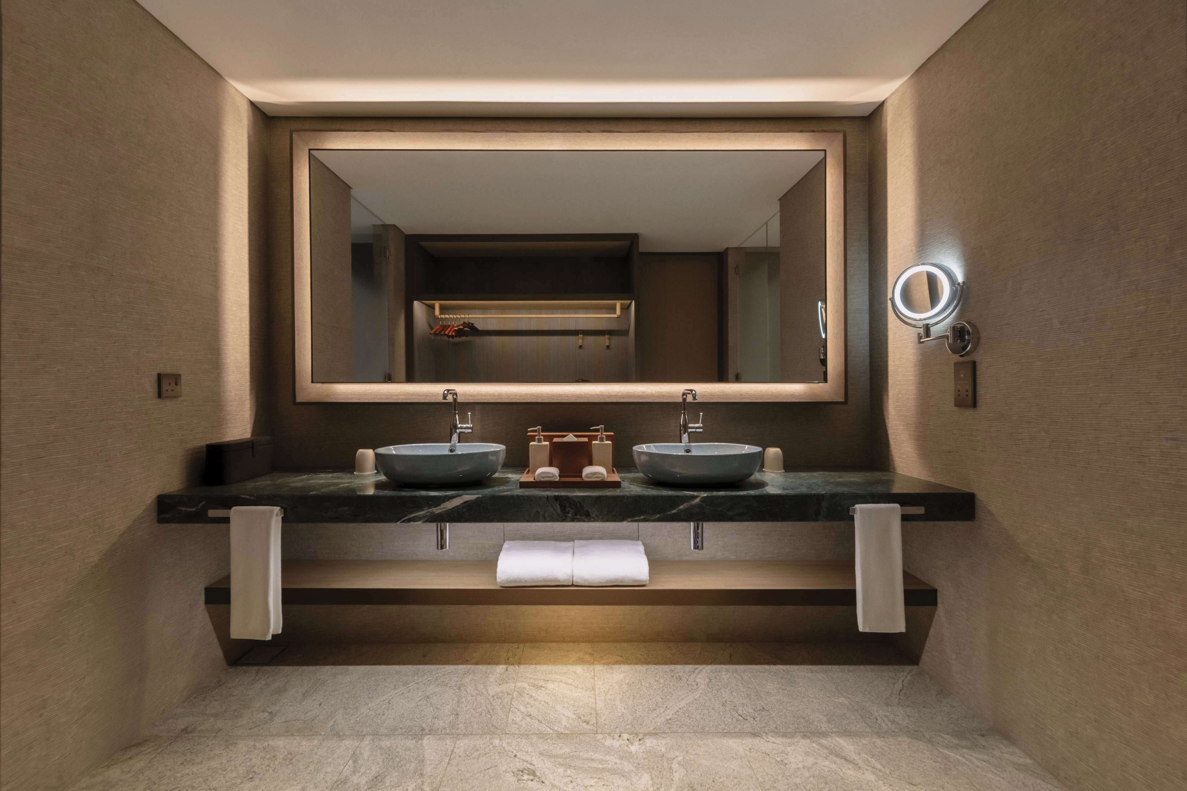 A modern bathroom with a large mirror, two sinks, and a towel rack.