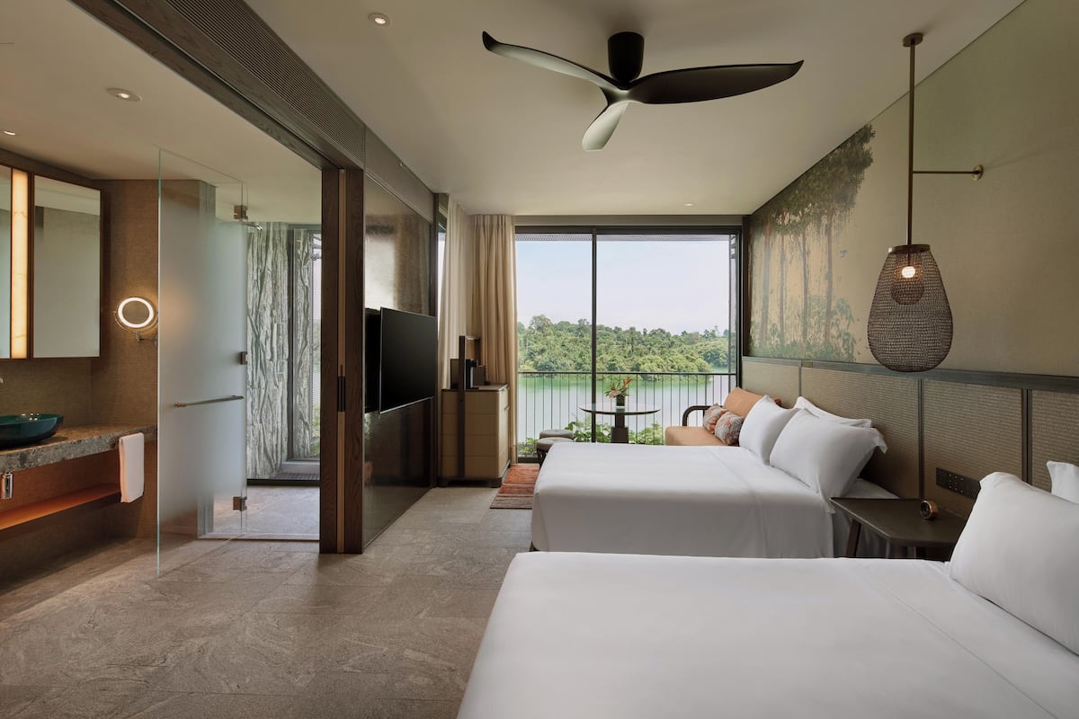 A hotel room with two beds, a TV, a bathroom with a mirror, and a view of the outdoors.