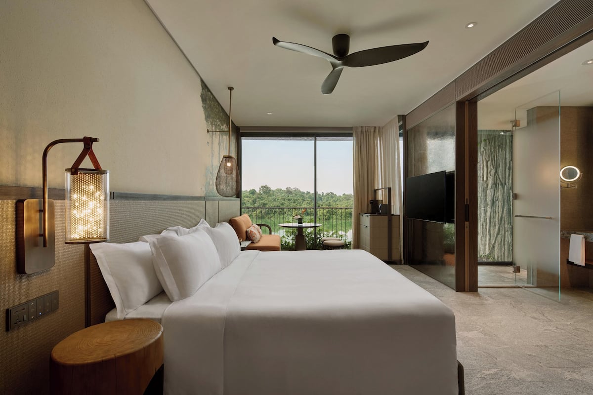 A modern hotel room with a large bed, a ceiling fan, a TV, and a balcony with a view.