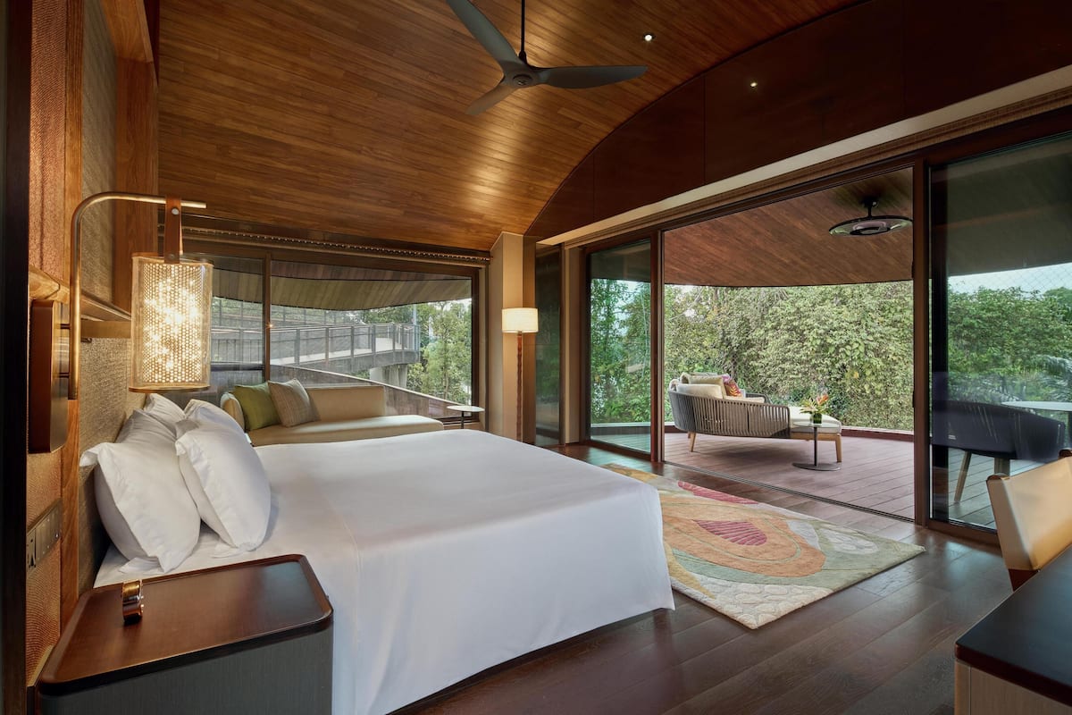 A spacious bedroom with a large bed, a desk, and a balcony with a view of the outdoors.