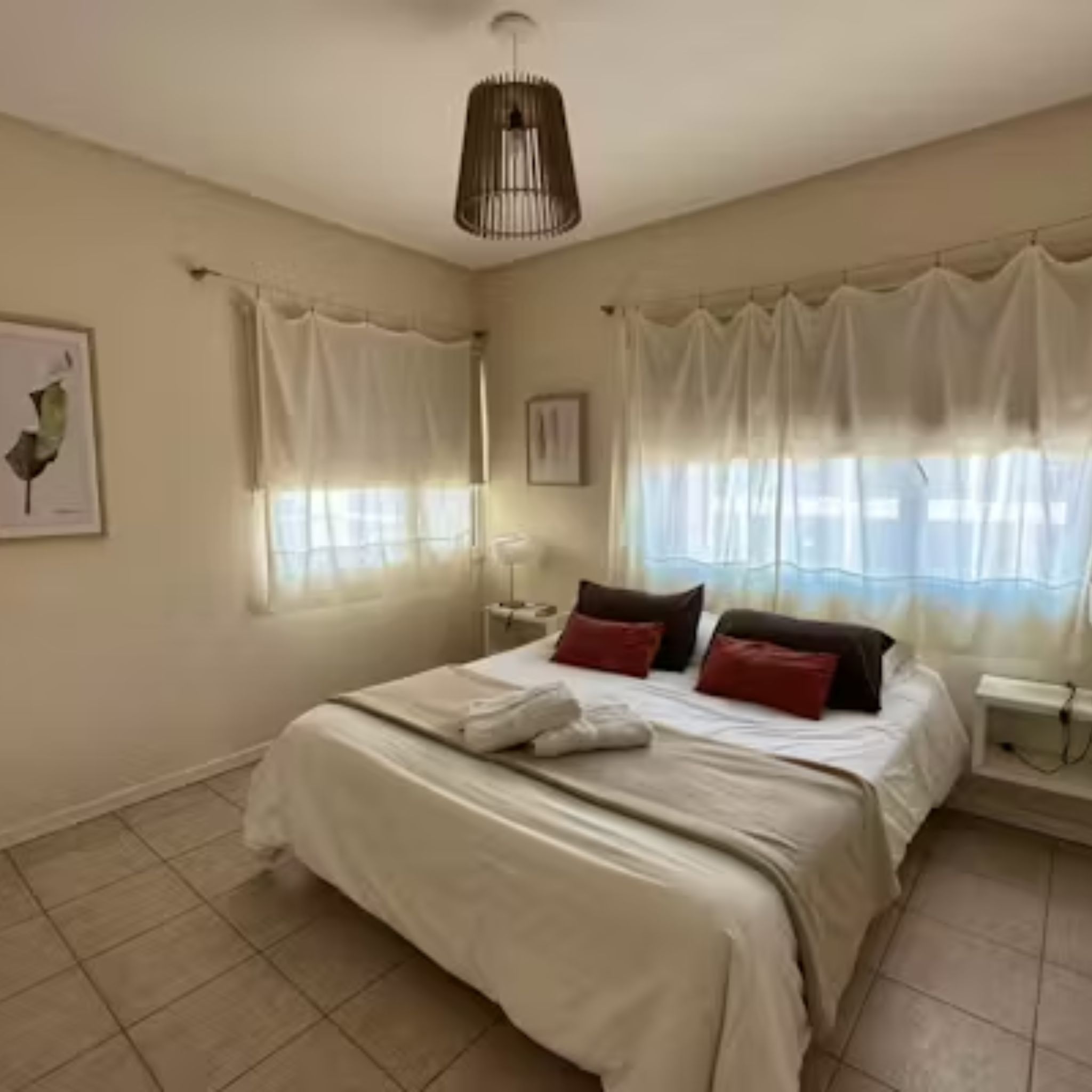 A bedroom with a bed, curtains, a bedside table, and a wall-mounted lamp.
