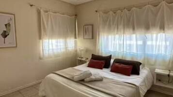 Un dormitorio con cama, cortinas, mesita de noche y una lámpara de pared.