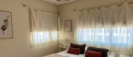 Une chambre à coucher avec un lit, des rideaux, une table de chevet et une lampe fixée au mur.