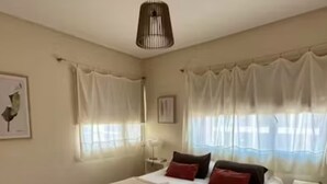 Une chambre à coucher avec un lit, des rideaux, une table de chevet et une lampe fixée au mur.