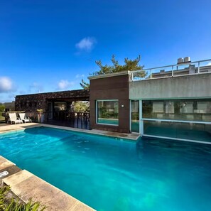 A modern pool area with a clear blue pool, lounge chairs, and a contemporary building with large windows. - Punto Playa (Villa Gesell)