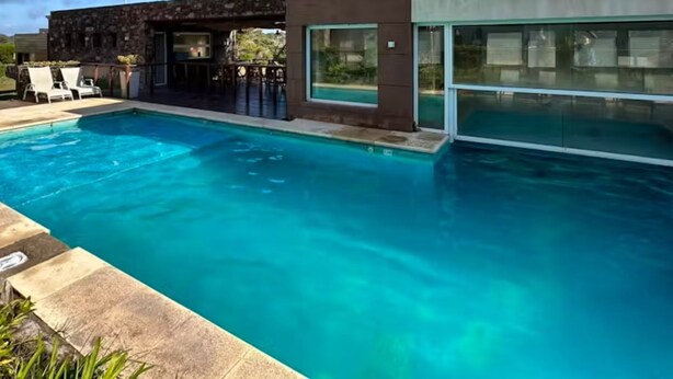 Un espace piscine moderne avec une piscine à l’eau cristalline, des chaises longues et un bâtiment contemporain doté de grandes fenêtres.