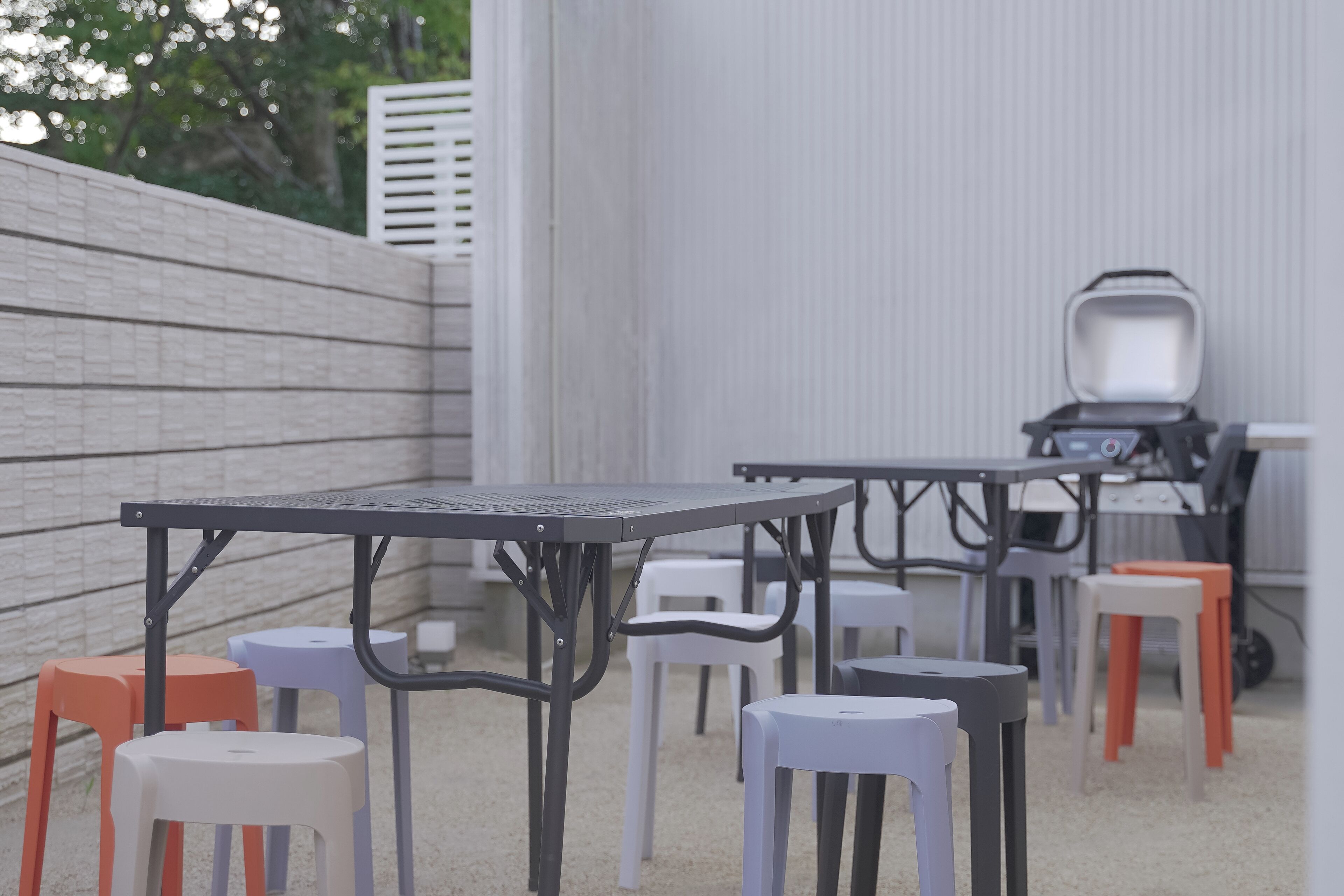 Un'area patio con tavoli e sedie da esterno, un barbecue e un muro bianco.