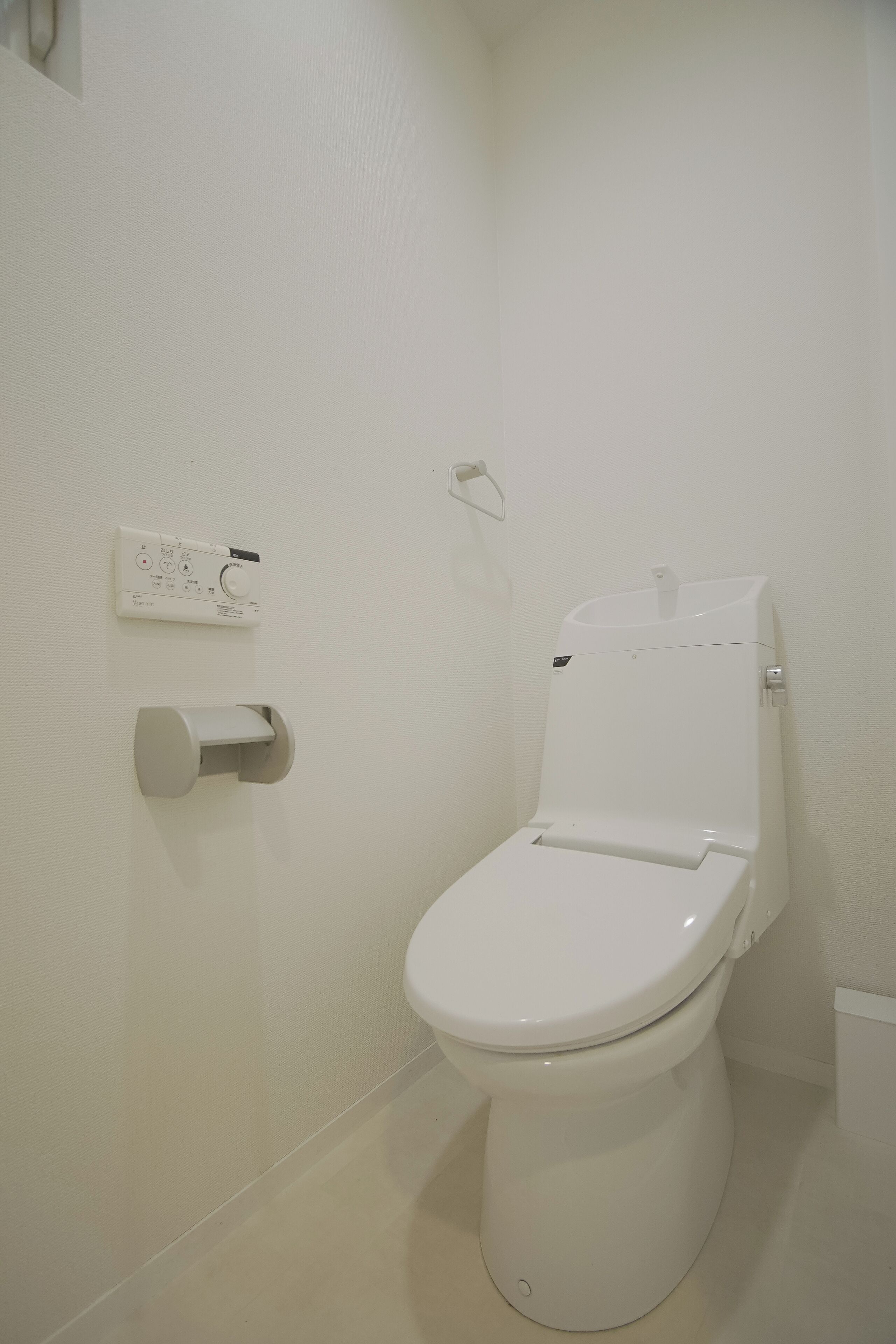Een wit toilet met een spoelknop en een papieren handdoekdispenser op de muur.