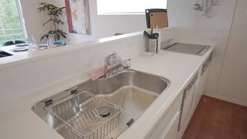 A modern kitchen with a stainless steel sink, a dish drying rack, and a window with a view of greenery.