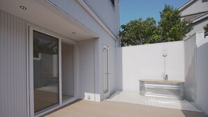 A modern outdoor patio with a wooden deck, a glass sliding door, and a built-in spa tub. - INOVE VILLA RITTO (Ritto)