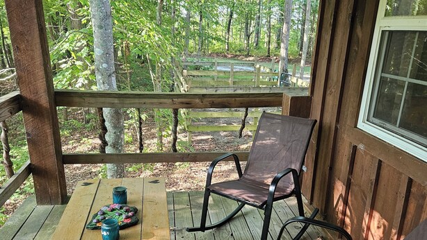 A wooden deck with a table and two chairs, overlooking a forested area.