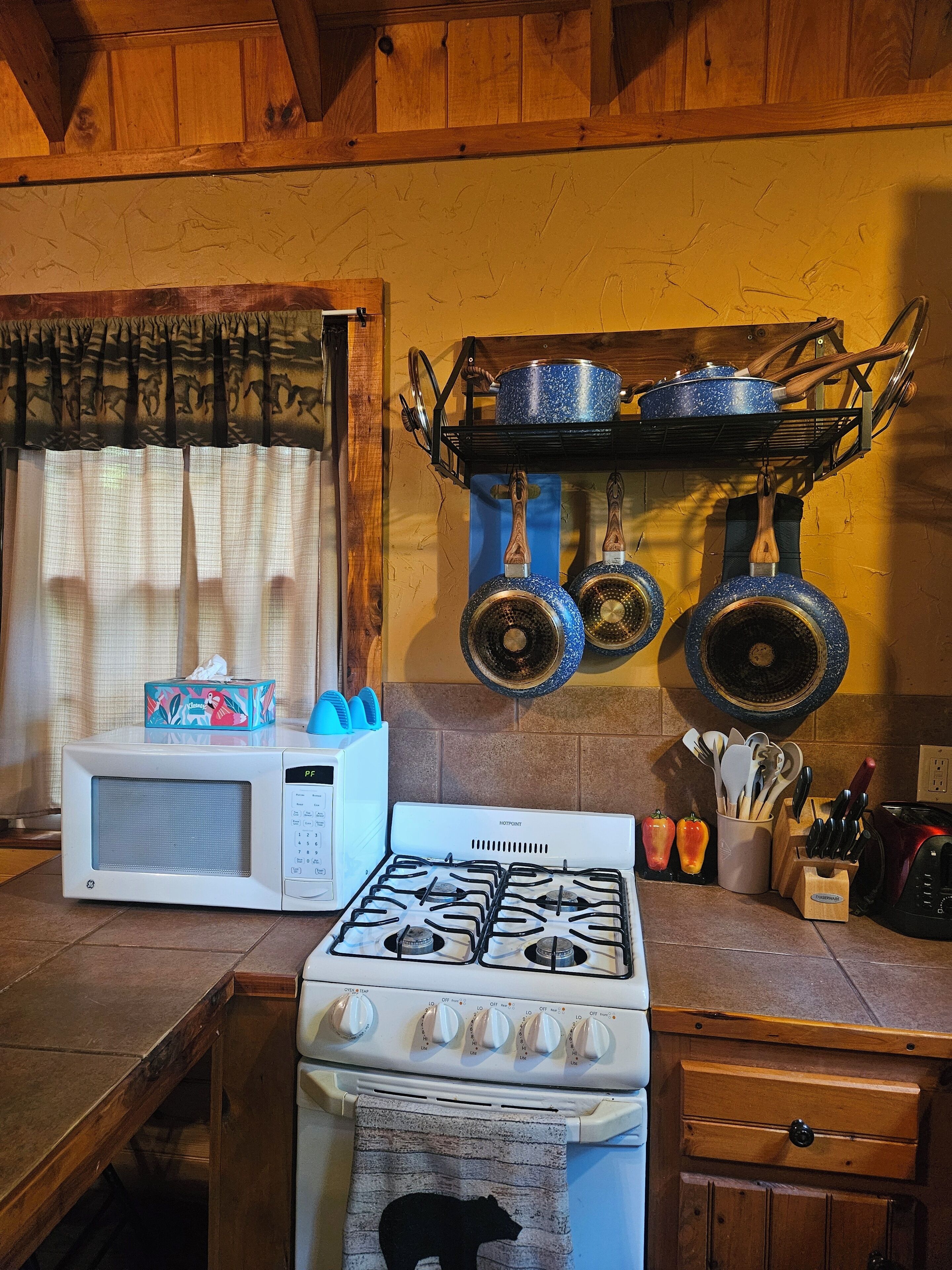A kitchen with a white stove, a microwave, and a wooden cabinet. There are pots hanging on the wall and a box of tissues on the counter.