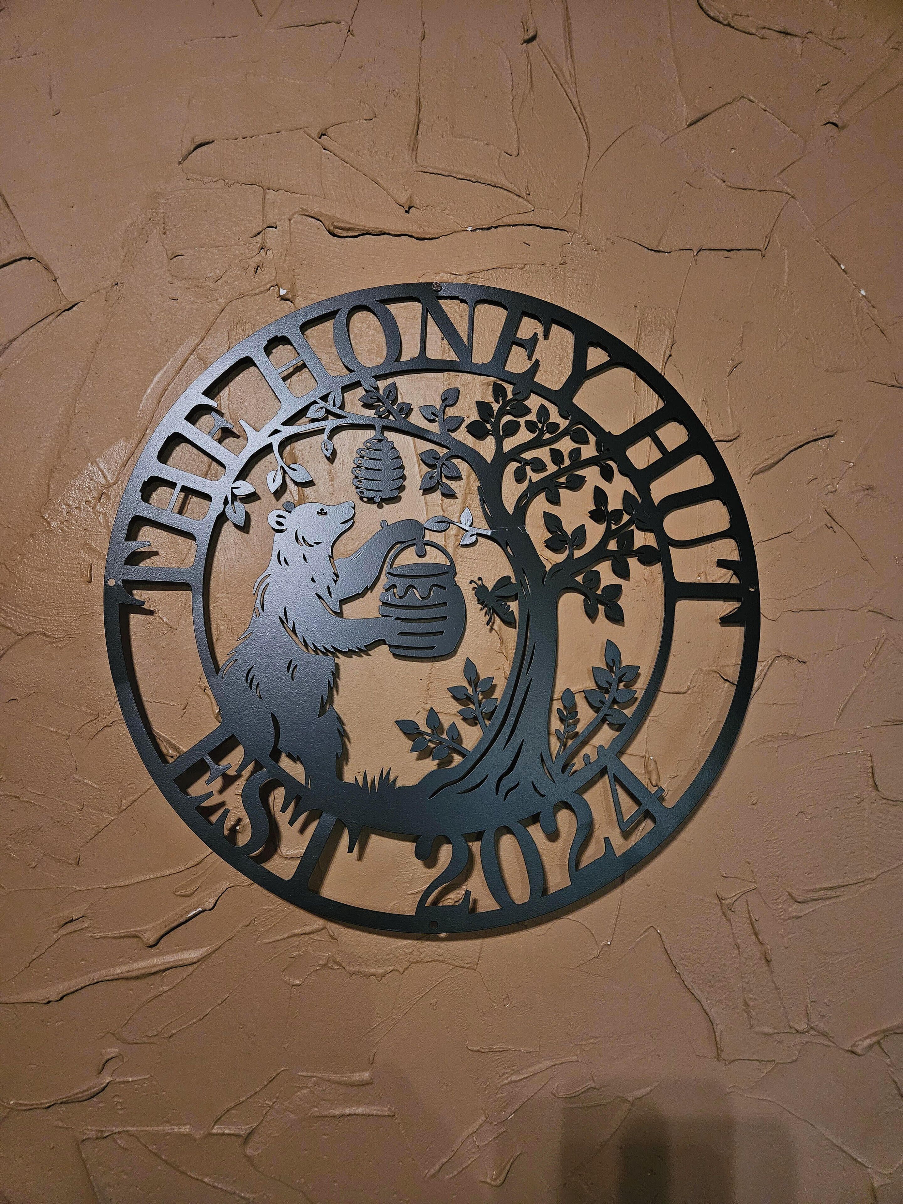 Une découpe circulaire en métal représentant un arbre et un ours, ainsi que le texte « VETTONEXY » et « 2012 » sur un mur texturé.