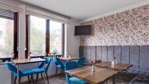 Ein Essbereich mit Holztischen und blauen Stühlen, einer grau gepolsterten Bank und einem an der Wand befestigten Fernseher.