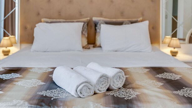 A neatly made bed with rolled white towels, a patterned bedspread, and a tufted headboard. - Oberhausen Cozy Nest (Oberhausen)