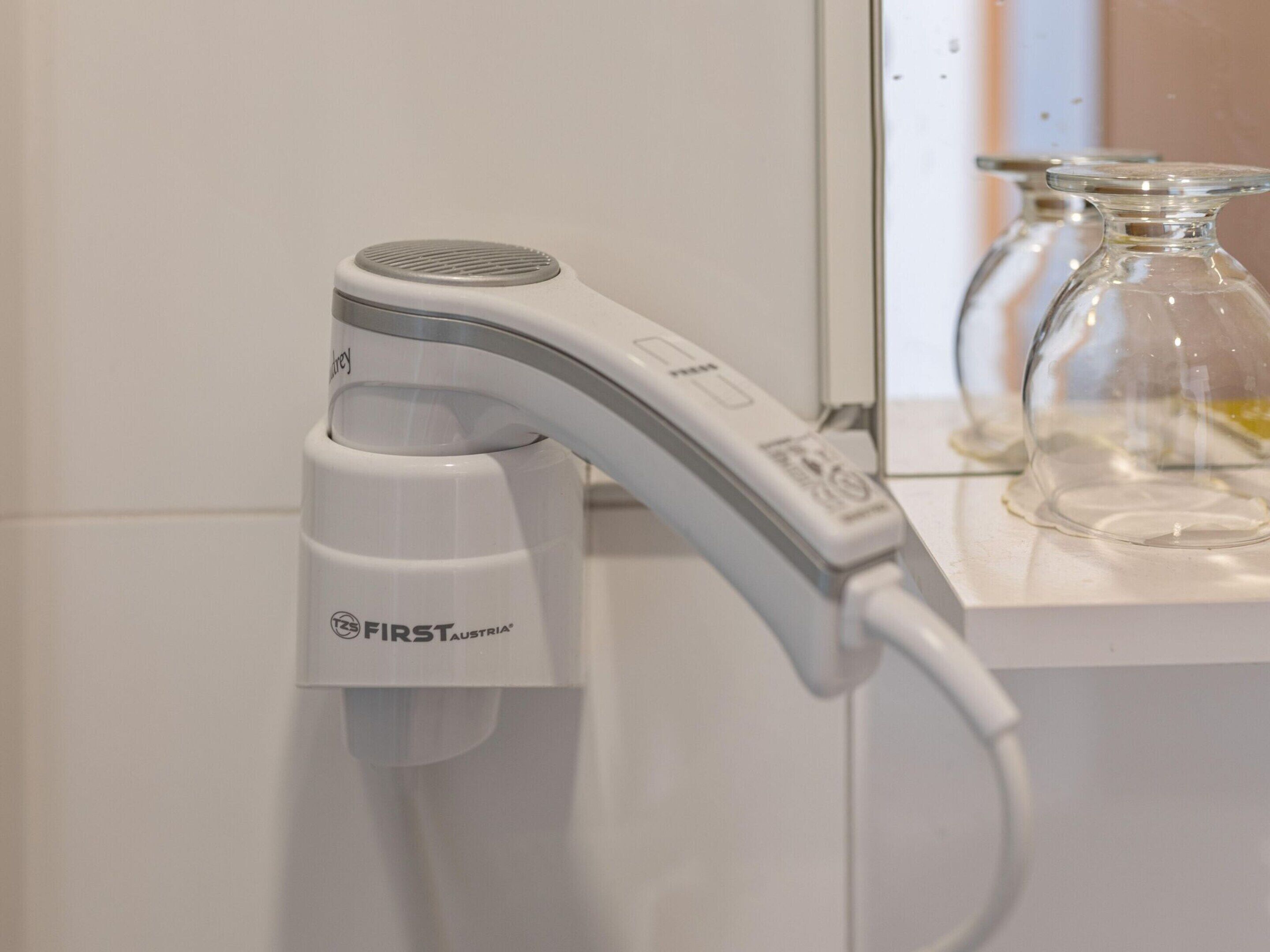 A white hair dryer with a cord, labeled "FIRST AUSTRIA," attached to a bathroom counter.