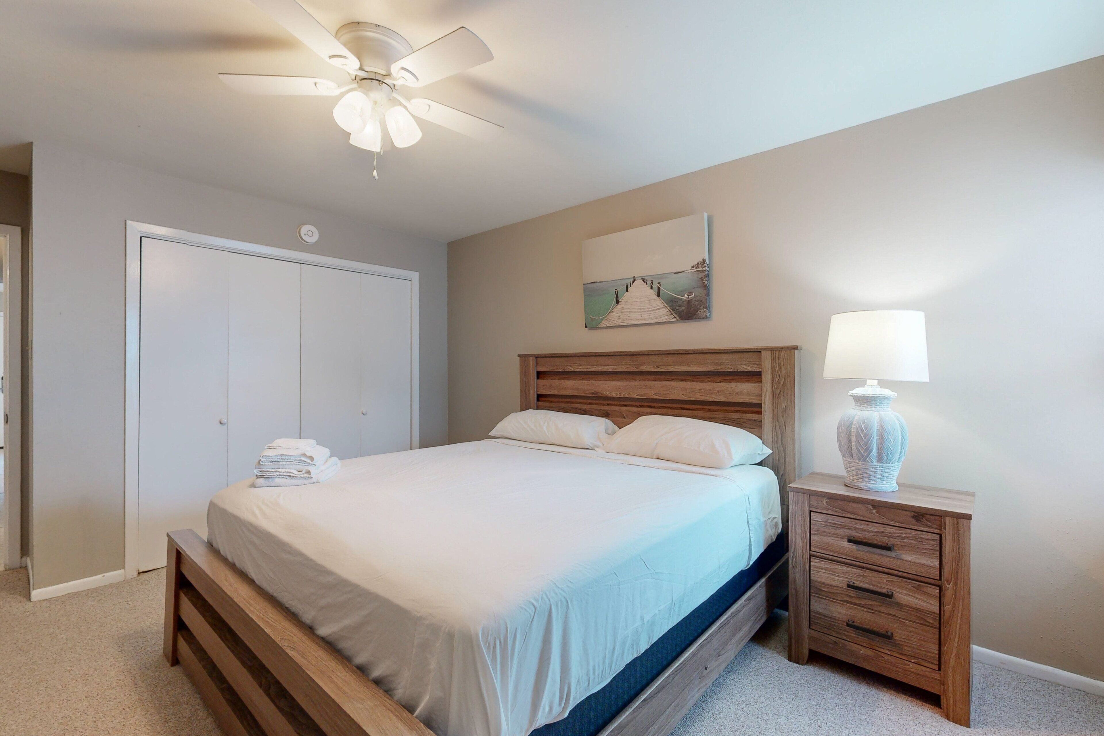 Une chambre à coucher avec un lit, une table de chevet, une lampe, un ventilateur de plafond et une porte.
