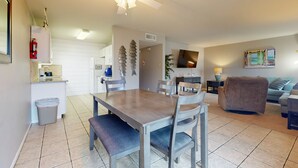 A dining area with a table and chairs, a ceiling fan, and a kitchen area in the background. - Beach Access Across the Street, Shared Heated Pool (Corpus Christi)