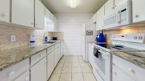 A compact kitchen with white cabinets, a granite countertop, a microwave, a kettle, and a dishwasher. - Beach Access Across the Street, Shared Heated Pool (Corpus Christi)