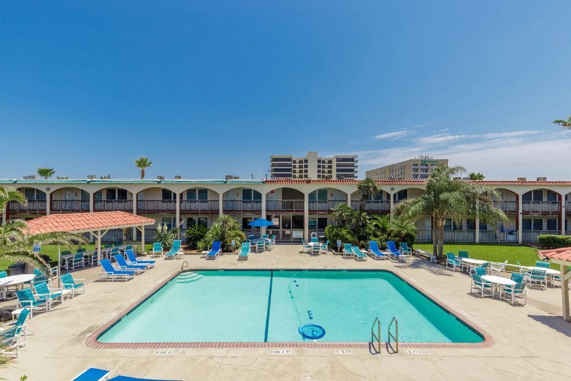 A hotel with a large pool area, multiple lounge chairs, and a building with balconies.