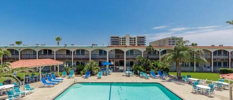 A hotel with a large pool area, multiple lounge chairs, and a building with balconies.