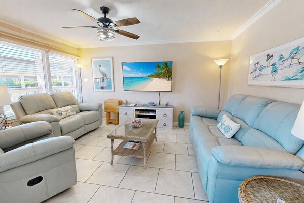 A living room with a sofa, a coffee table, a TV, and artwork on the wall. - Beach Access Across the Street, Shared Heated Pool, Pet Friendly (Corpus Christi)