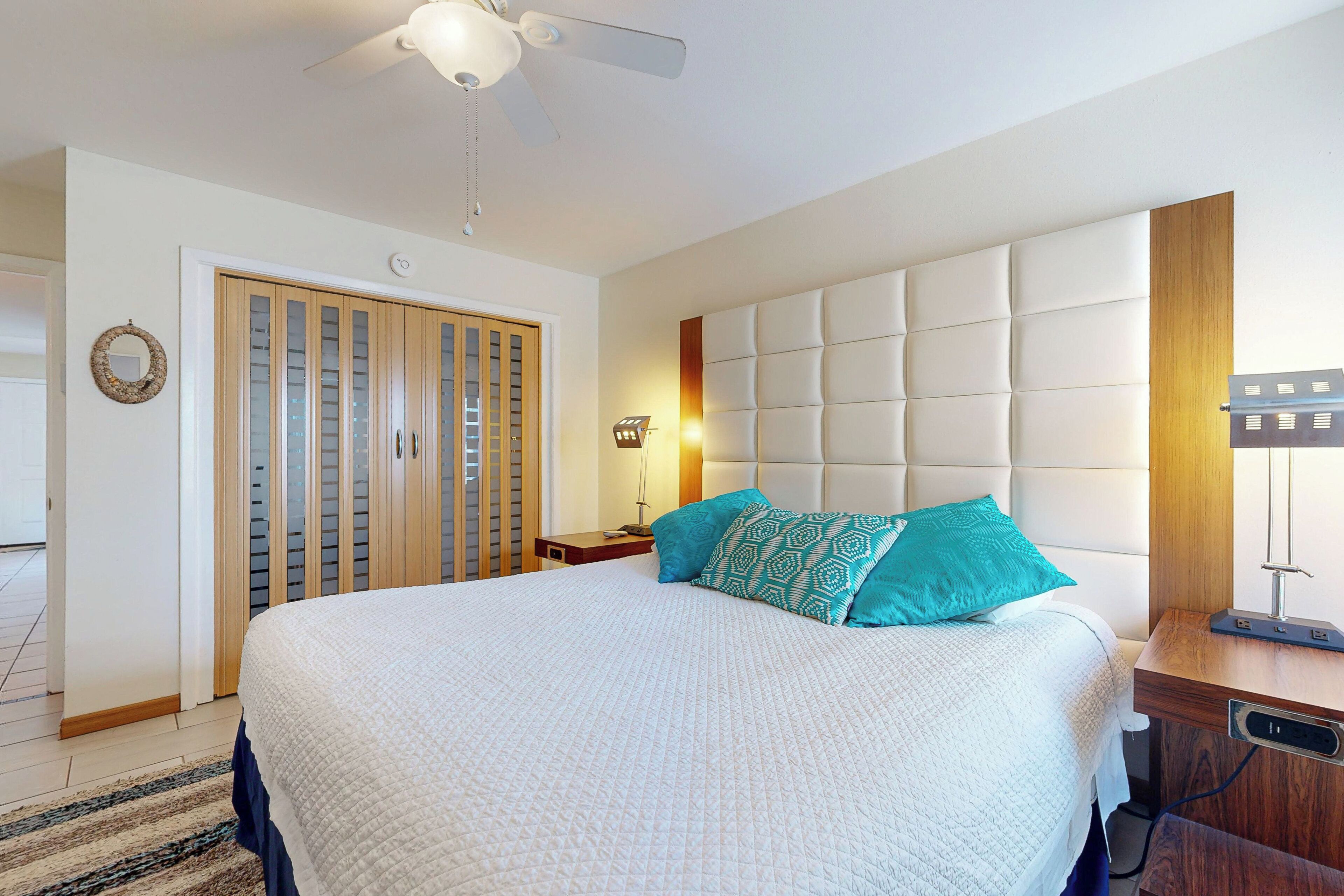 A neatly arranged bedroom with a large bed, a ceiling fan, a wardrobe, and a bedside table.