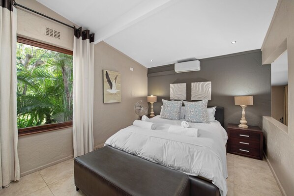Une chambre moderne avec un grand lit, une table de chevet, un banc et une fenêtre avec des rideaux.