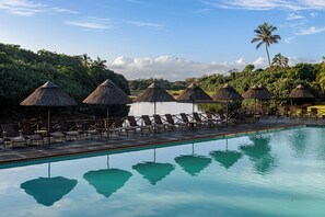 A poolside area with lounge chairs and thatched umbrellas, surrounded by lush greenery and palm trees. - San Lameer Villa 3216 (Southbroom)