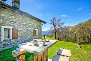 Ein Steinhaus mit einem Steintisch im Freien, einer Holzbank und Blick auf die Berge.
