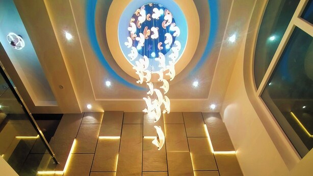 Un intérieur moderne avec un luminaire central, un plafond orné de motifs et un sol carrelé.