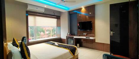 A modern hotel room with a large bed, a TV, a desk, and a window with blinds.