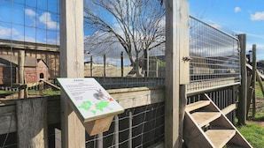 A wooden fence with a metal gate, a wooden staircase, and a sign with a map and text.
