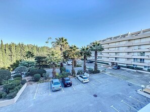 A parking lot with several cars, surrounded by palm trees and a building with multiple balconies. - Apart 4 p, sea view, terraces, swimming pool, A/C (Saint-Raphaël)