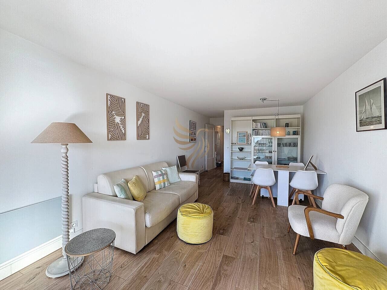 Un soggiorno moderno con divano, poggiapiedi e poltrone, una zona pranzo con tavolo e sedie, e una cucina sullo sfondo.