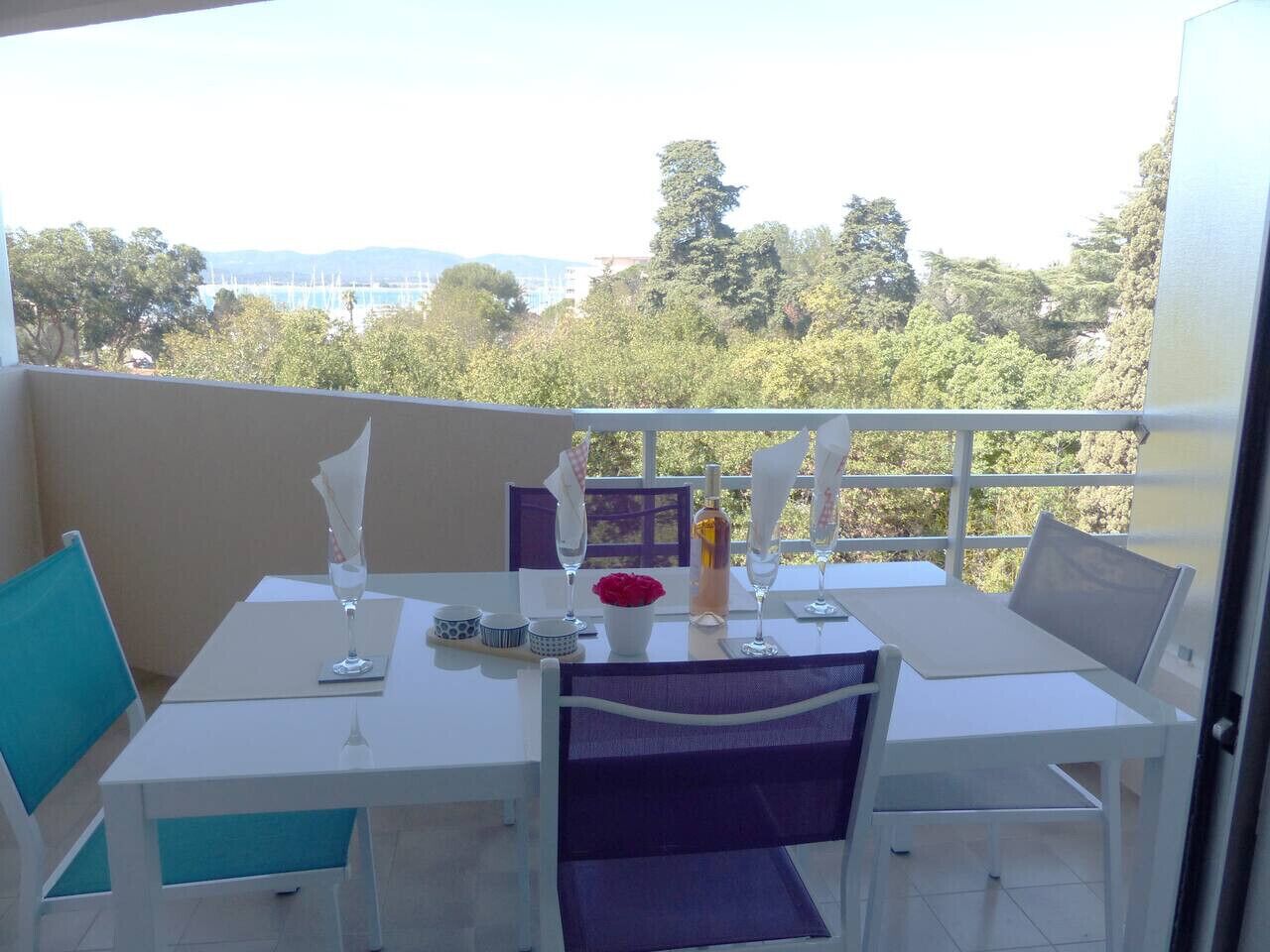Un balcone con un tavolo apparecchiato per due, vista su alberi ed edifici in lontananza.
