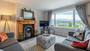 A living room with a fireplace, a television, and a large window with a view. - 2 bedroom home in Kenmare with sea views to sleep 4 (Kenmare)
