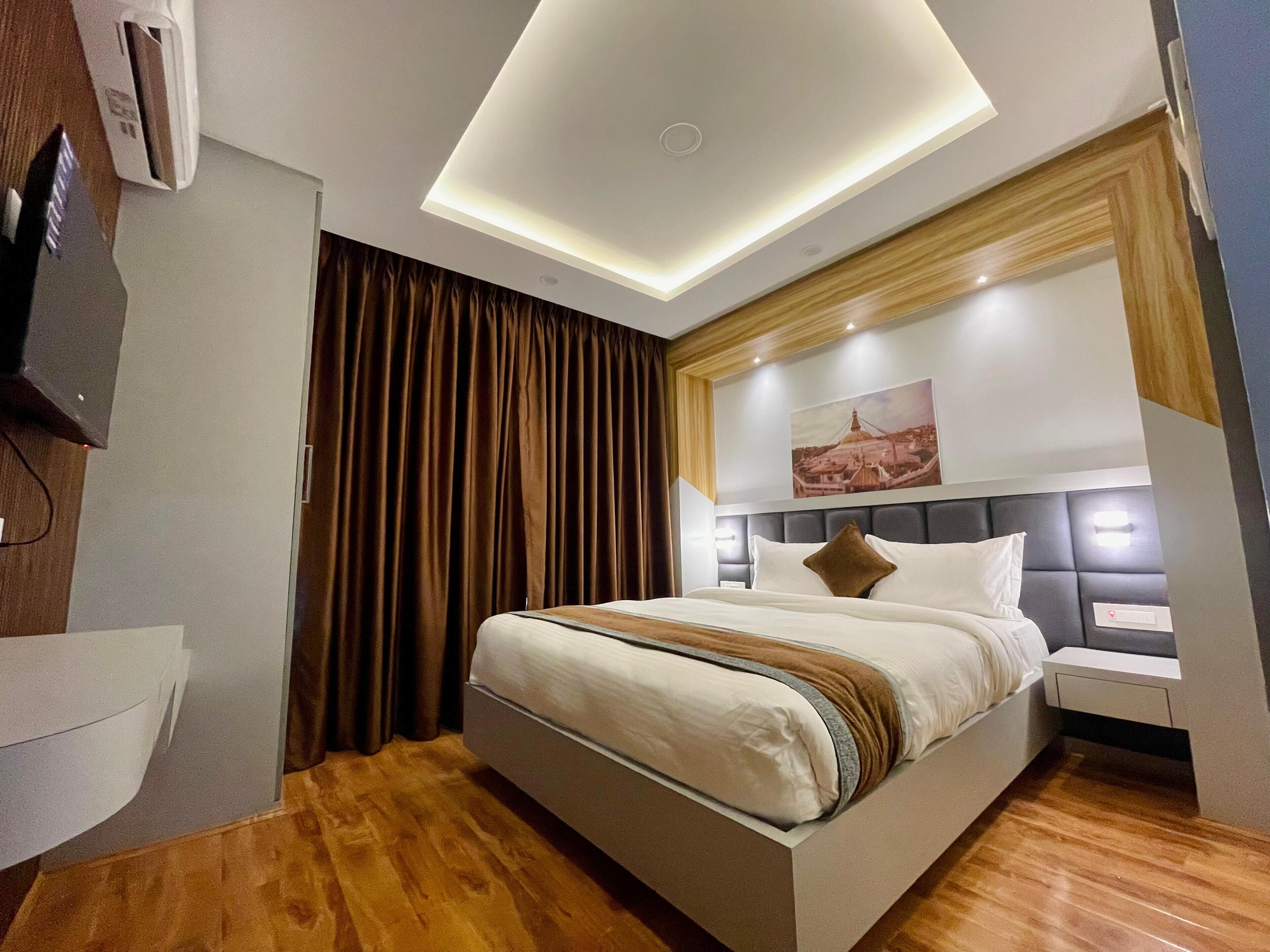 Une chambre d’hôtel moderne dotée d’un grand lit, d’une tête de lit avec éclairage intégré, d’un luminaire au plafond et d’un tableau encadré au mur.
