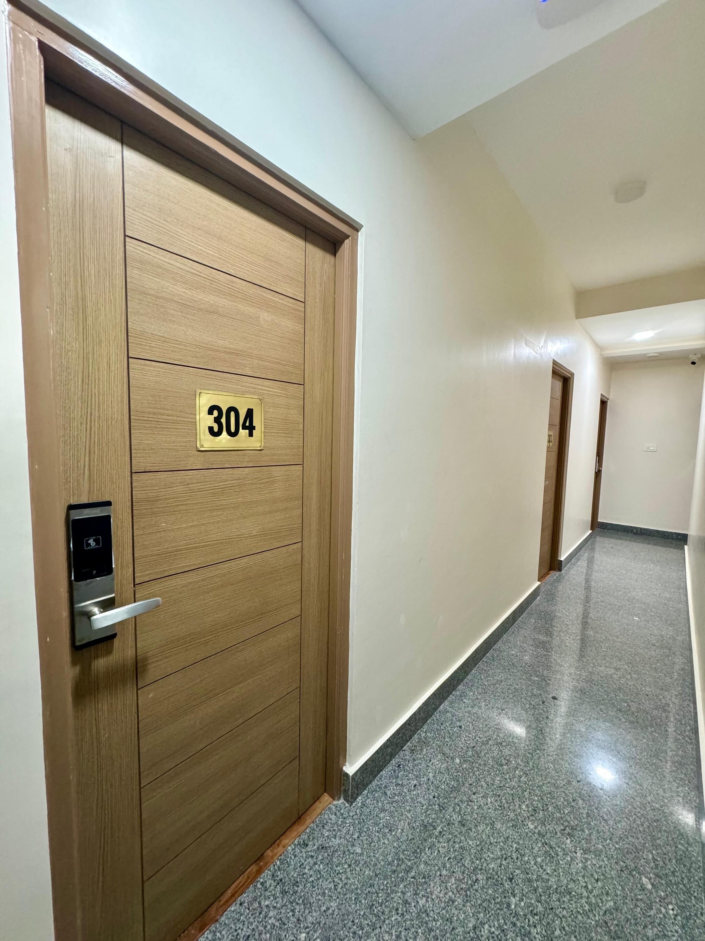 A hallway with a wooden door marked with the number 304, a modern door handle, and a security camera on the ceiling.