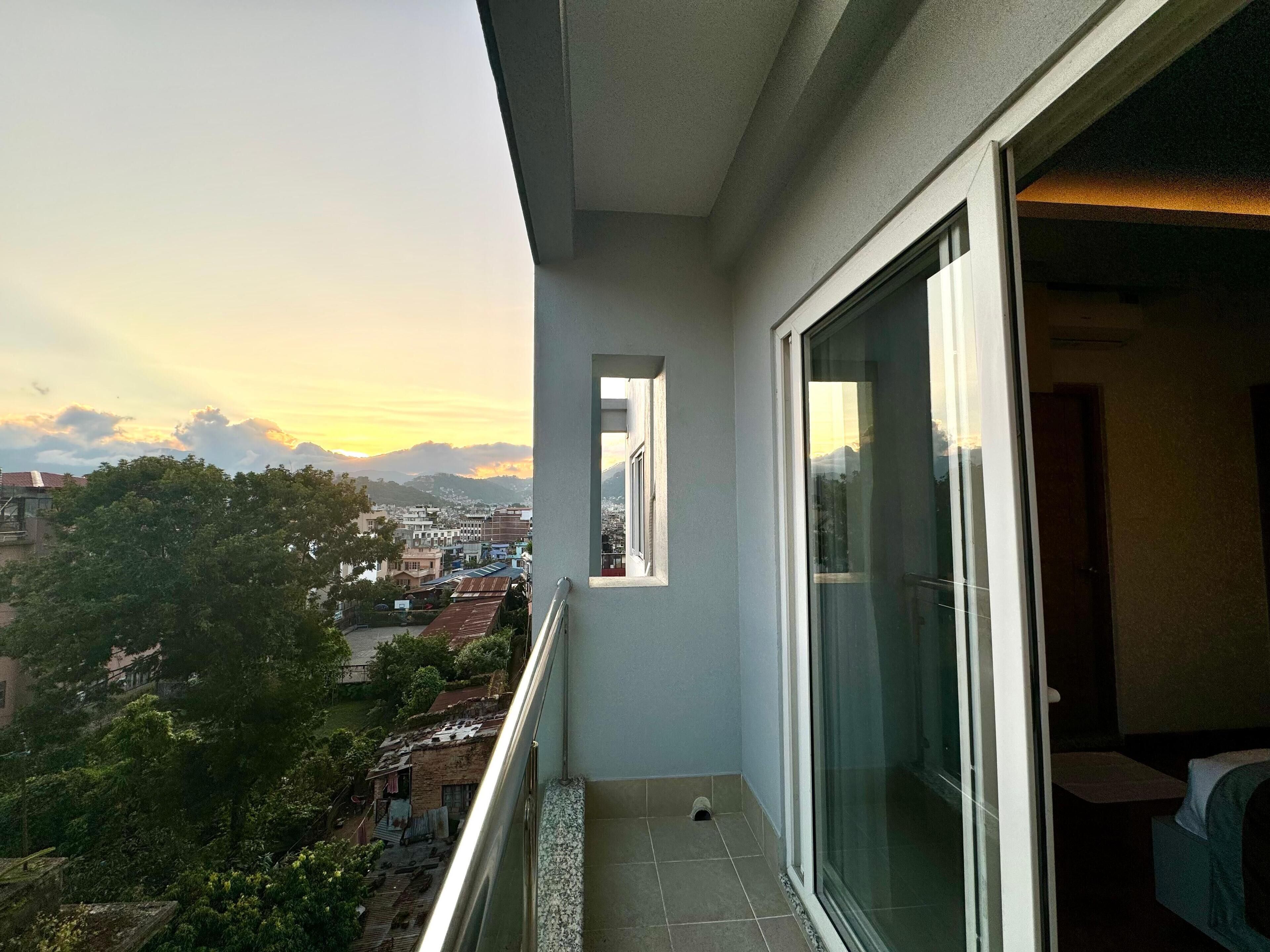 Varanda com vista para uma paisagem urbana e montanhas ao pôr do sol.