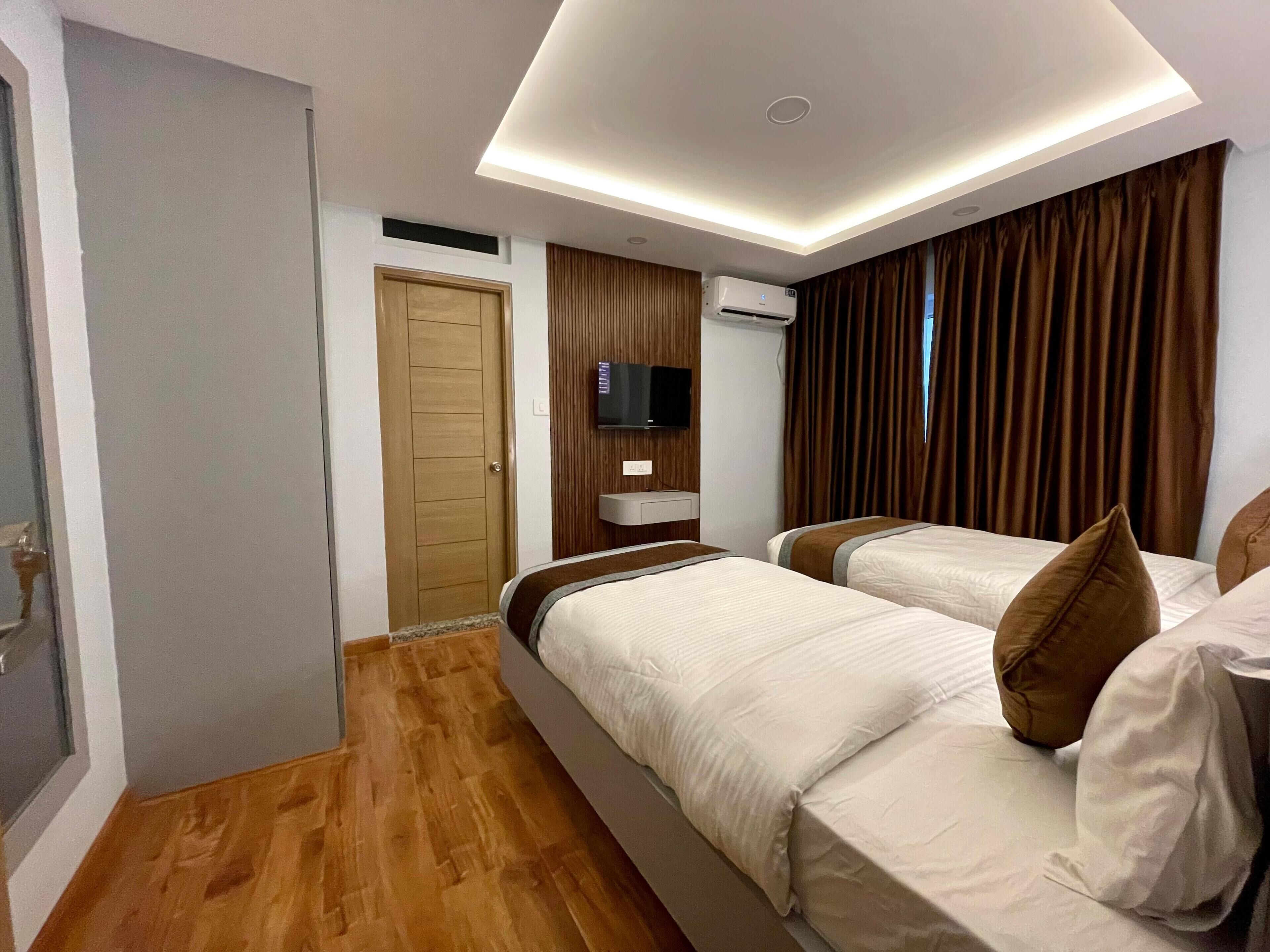 A hotel room with two beds, a TV mounted on the wall, an air conditioning unit, and a wooden door.