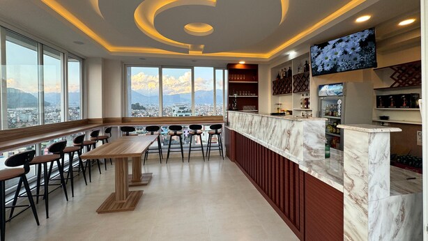 A modern bar with a marble countertop, wooden chairs, and a city view through large windows. - Hotel Alleyway Express (Kathmandu)