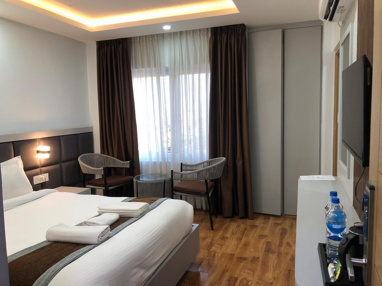 A hotel room with a bed, two chairs, a small table, a TV, and a water dispenser.