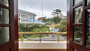 Vista desde un balcón con barandilla, suelo de baldosas y un edificio con techo azul al fondo.