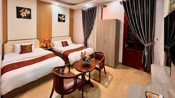 Una habitación de hotel con dos camas, un armario de madera, una mesita redonda con un jarrón de flores y una puerta roja.