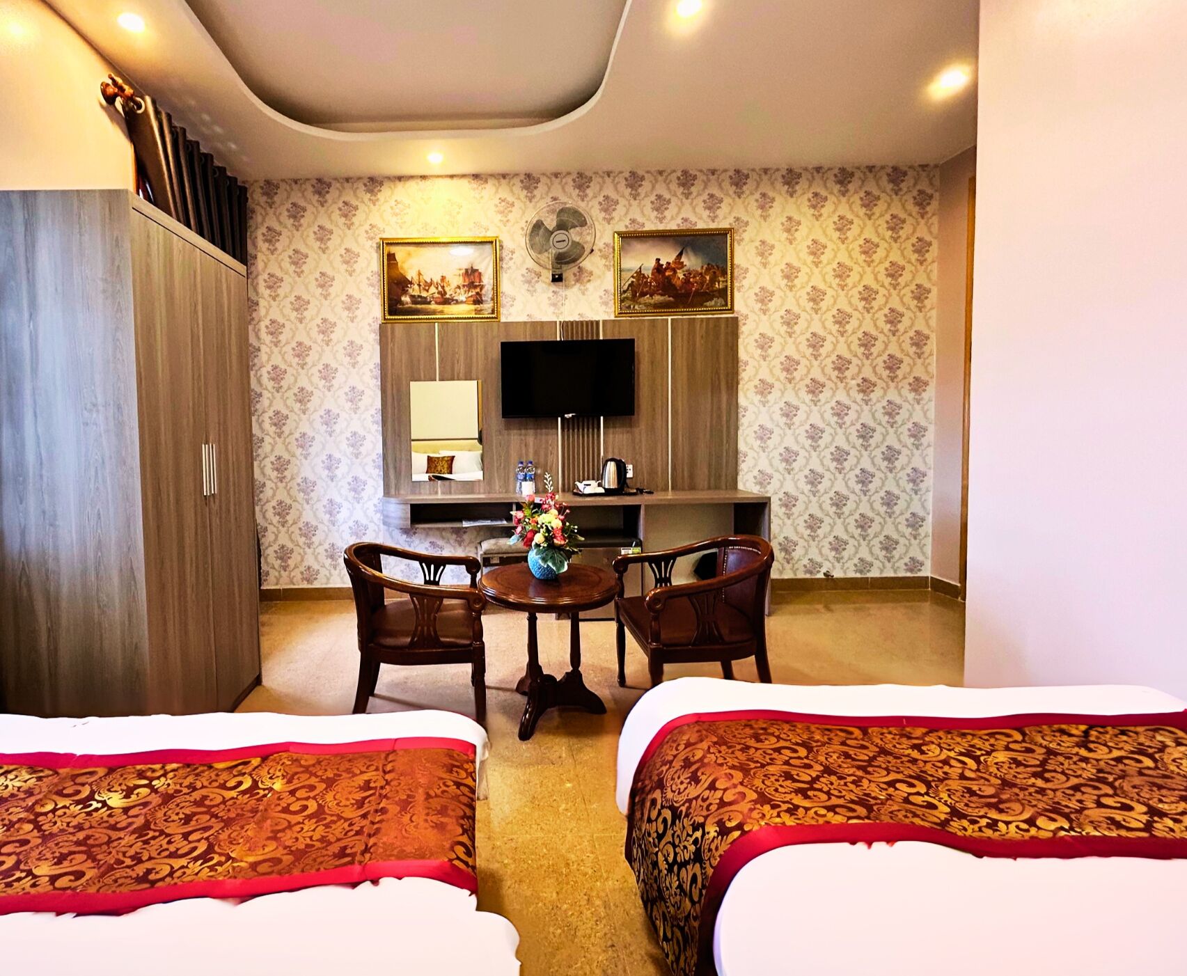 A hotel room with two beds, a dining table with chairs, a TV, and a minibar.