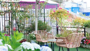Un patio con mobiliario de mimbre y una mesa, rodeado de plantas y flores en macetas.