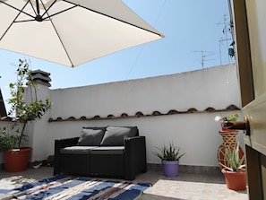 A balcony with a wicker sofa, a large umbrella, and potted plants.