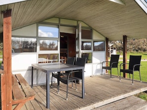 Un espace extérieur aménagé, abrité et doté d’une table et de chaises, de grandes fenêtres et d’une terrasse en bois.